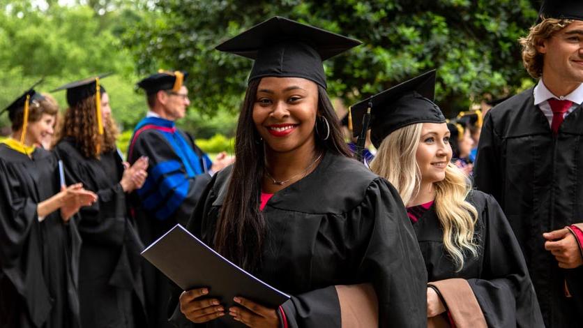 A student in the crowd smiles after receiving her diploma at commencement